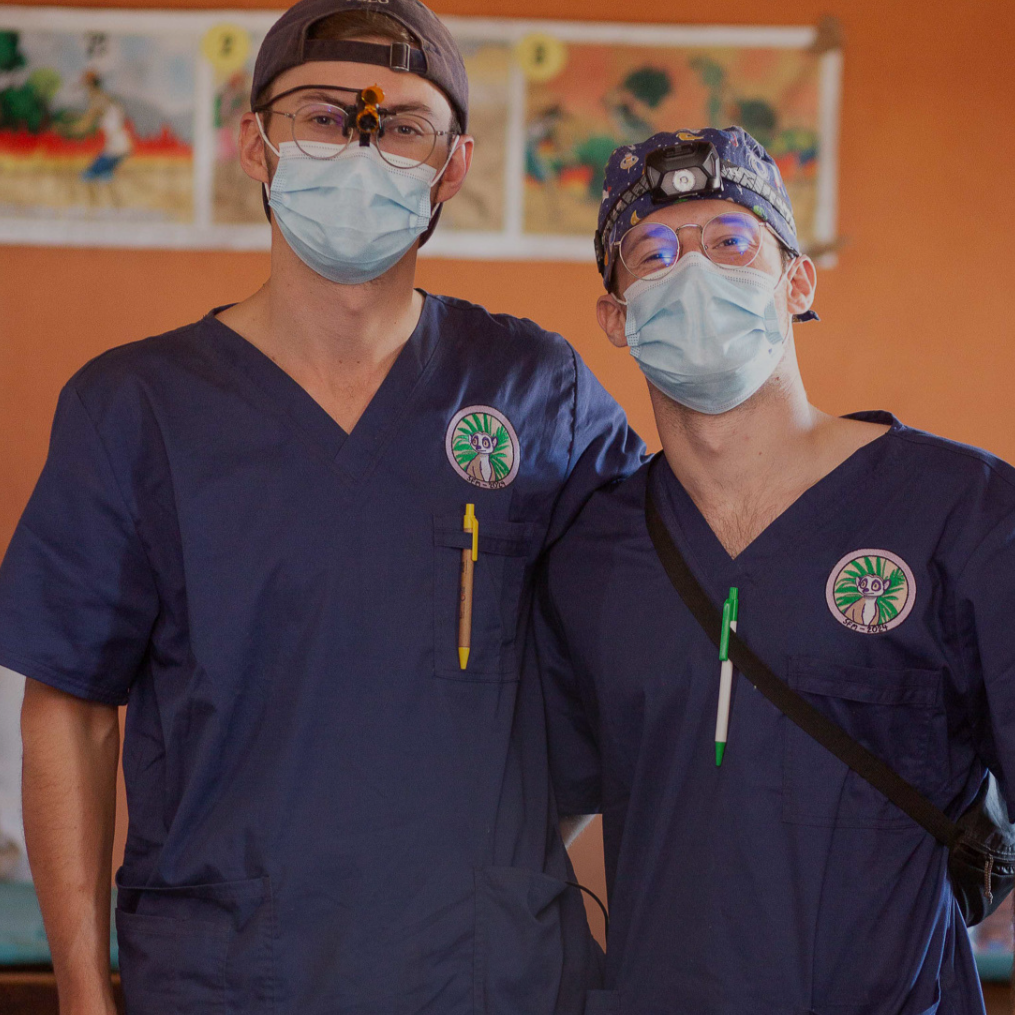 Two men in scrubs tops posing for picture while a volunteer trip